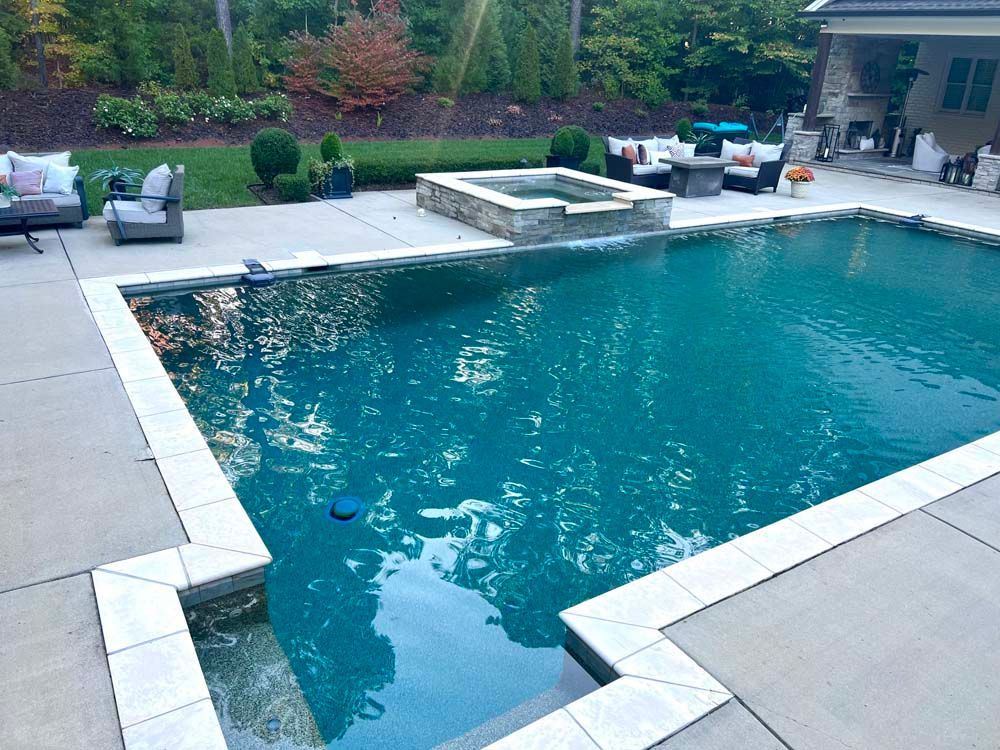 Rectangular pool with jacuzzi, patio seating. Green water, stone accents, and manicured landscaping.