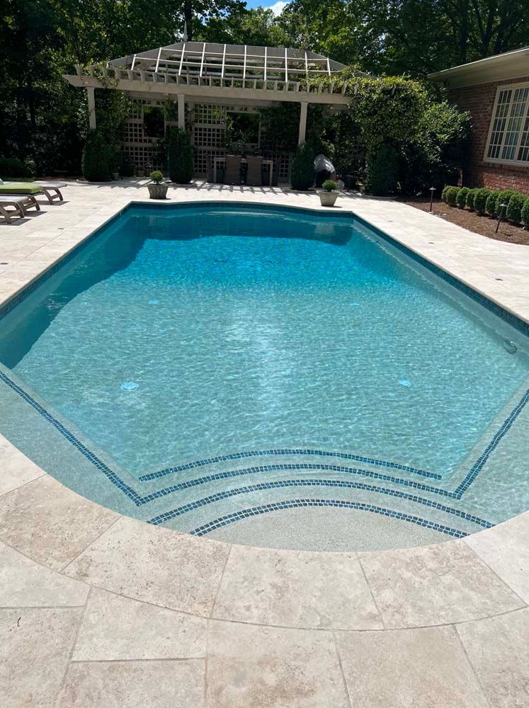 Swimming pool with blue water and steps, surrounded by stone patio and a white pergola.