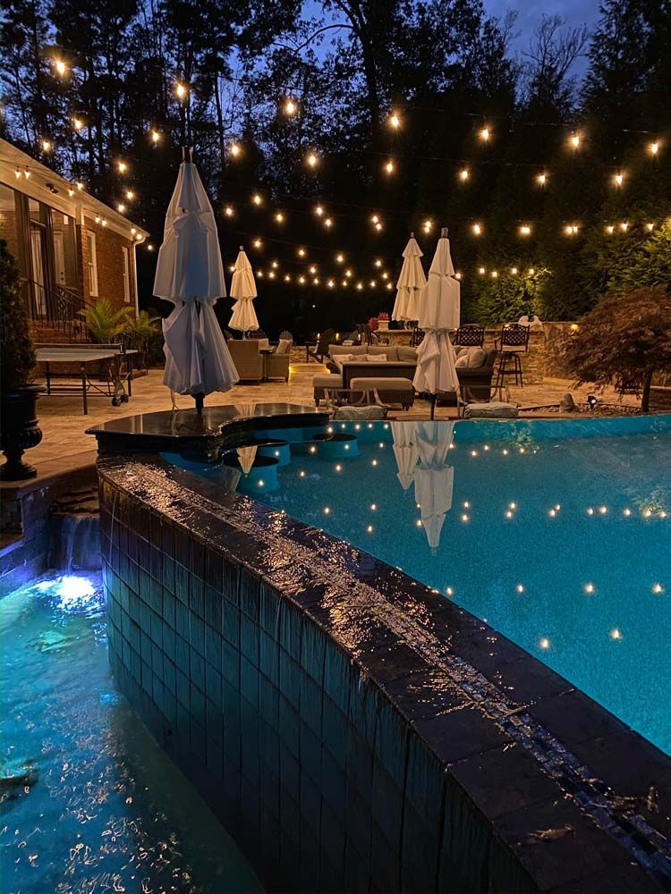 Poolside evening scene with string lights, white umbrellas, and reflecting water.