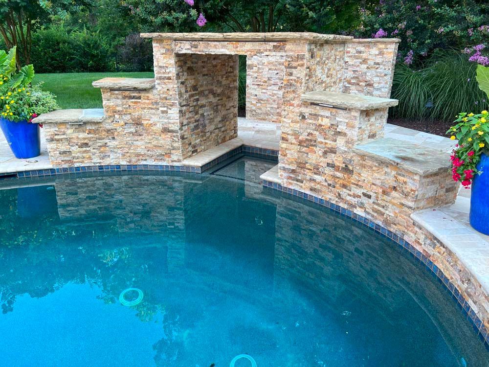 Pool with stone structure and built-in steps, blue water, blue planters, and green grass.