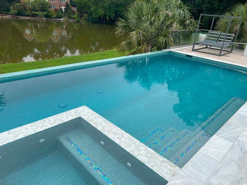 Pool with turquoise water, steps, and a hot tub. Overlooks a lake with a swing.