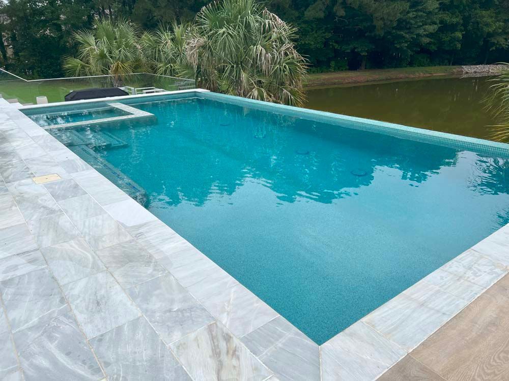 Swimming pool with turquoise water and white tile border. Overlooks a lake, trees in the background.