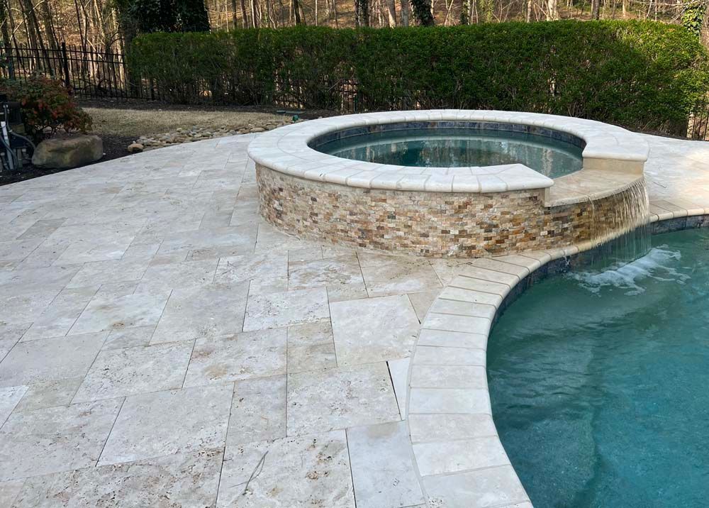 Poolside with hot tub and turquoise water, surrounded by light-colored paving stones.