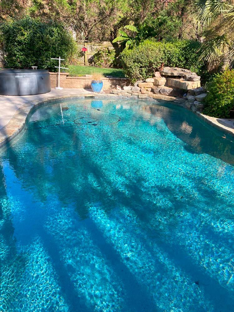 Swimming pool with turquoise water, hot tub, and lush greenery in a sunny outdoor setting.