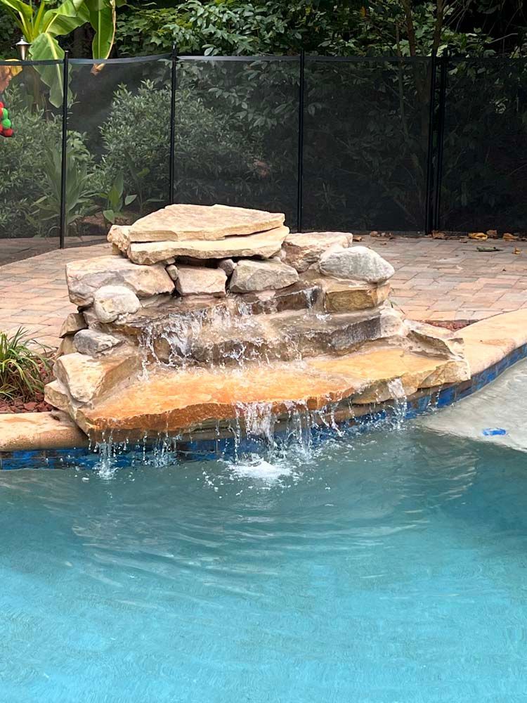 Waterfall feature cascading into a swimming pool; brown stone, clear water, blue pool.