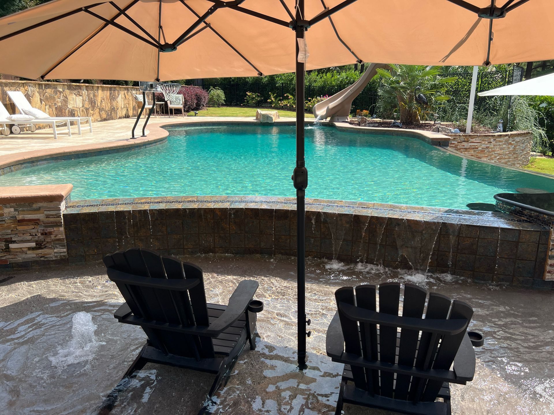 Two chairs under an umbrella next to a swimming pool
