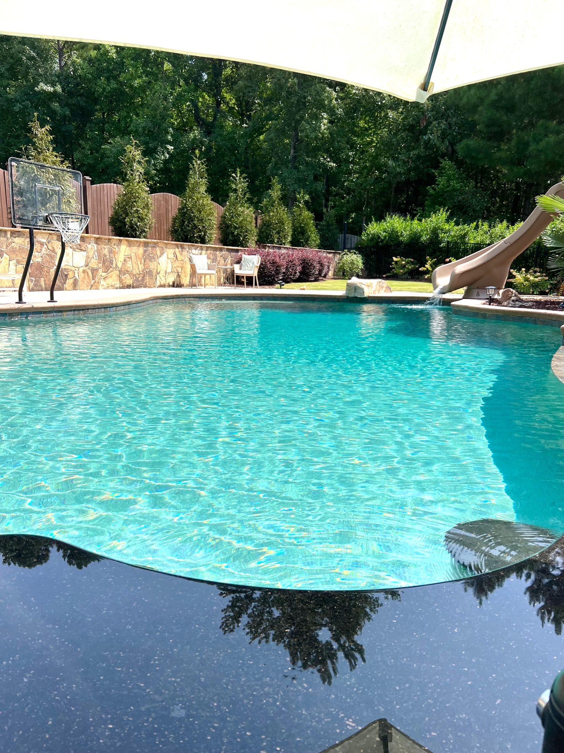 Swimming pool with turquoise water, a slide, and lush greenery in the background.