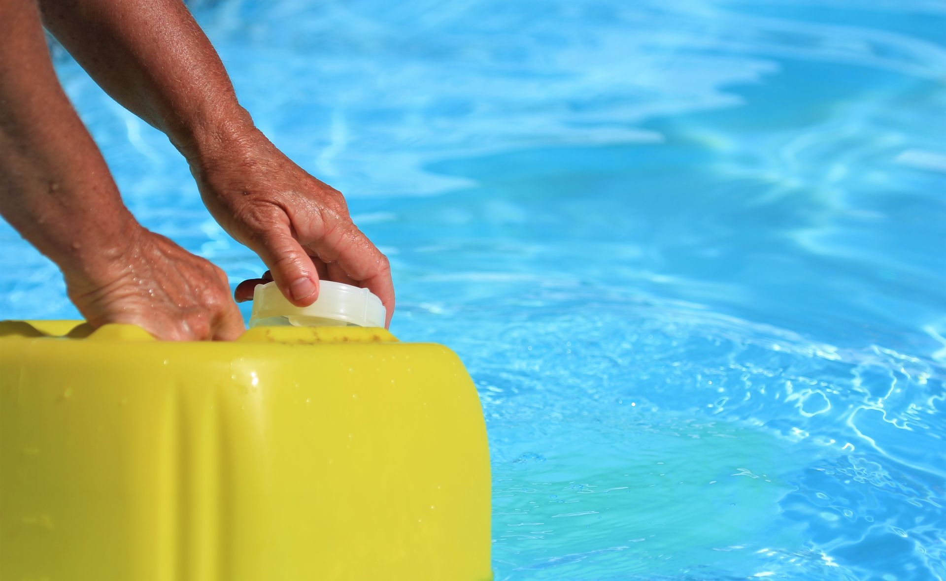 Hands opening a yellow container next to a pool.