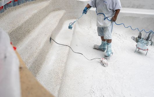 Worker spray-painting a white floor with a blue hose in a large room