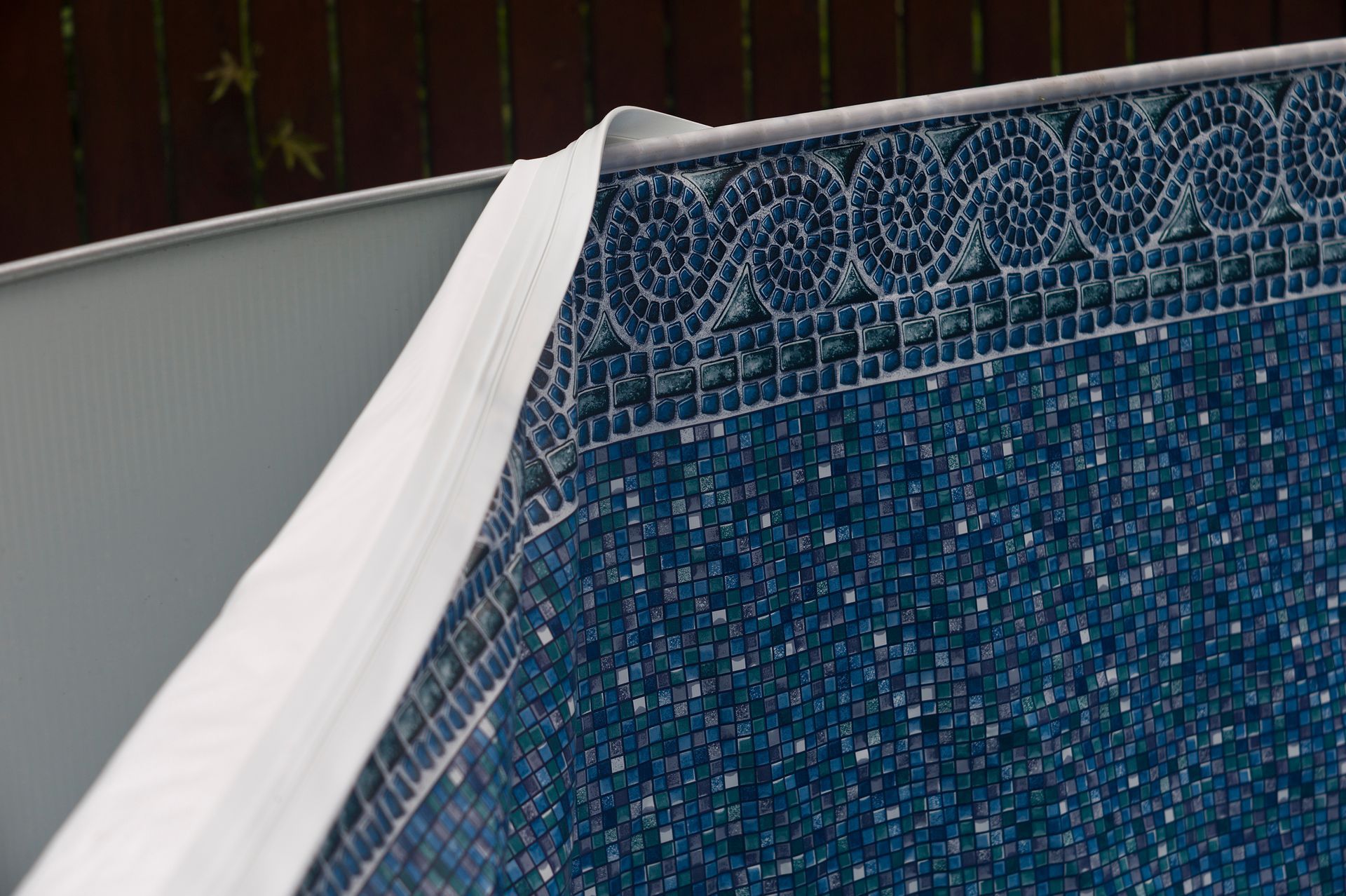 Pool liner partially peeled back, revealing a blue mosaic tiled wall.