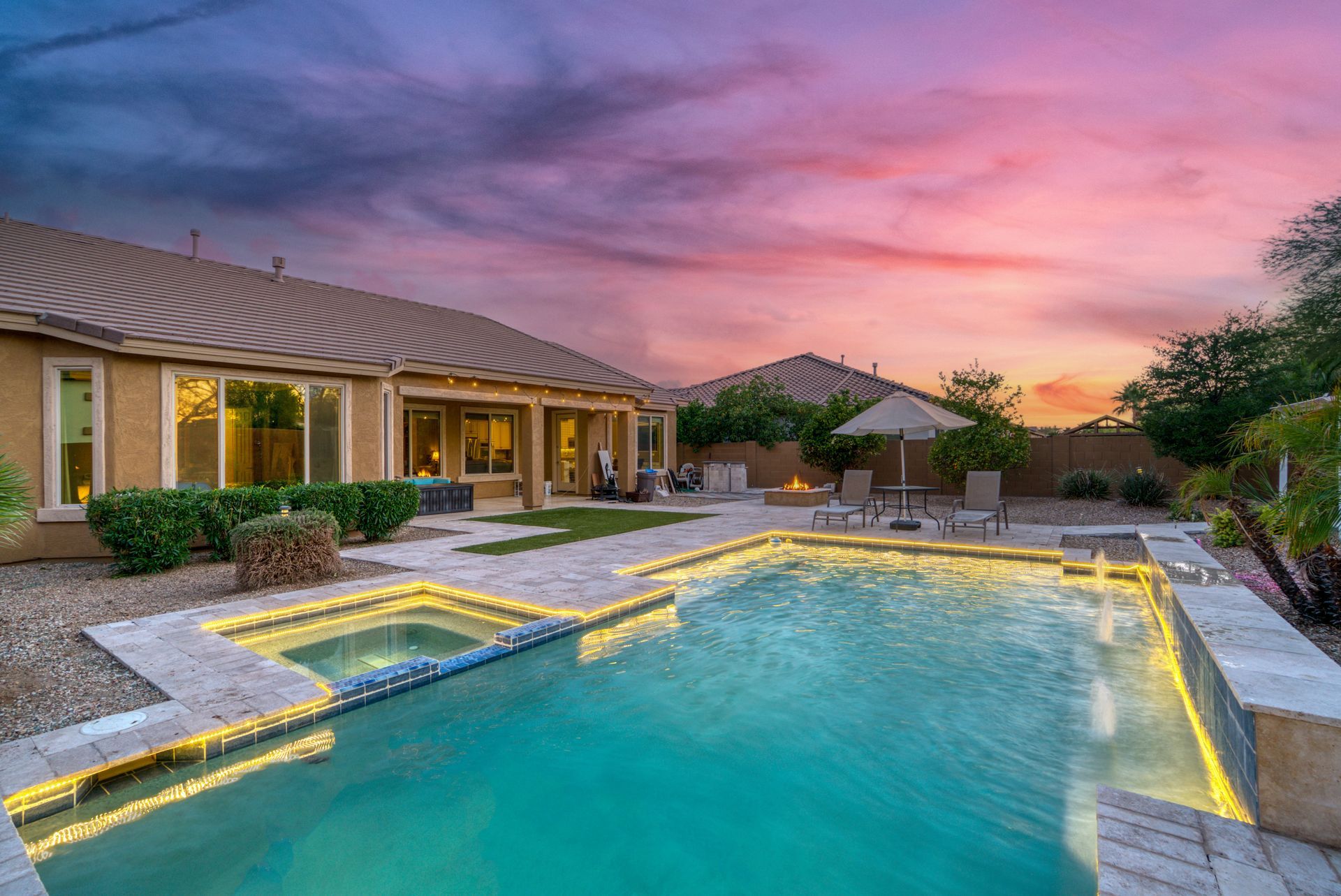 Backyard pool with spa, house in background, under colorful sunset sky.