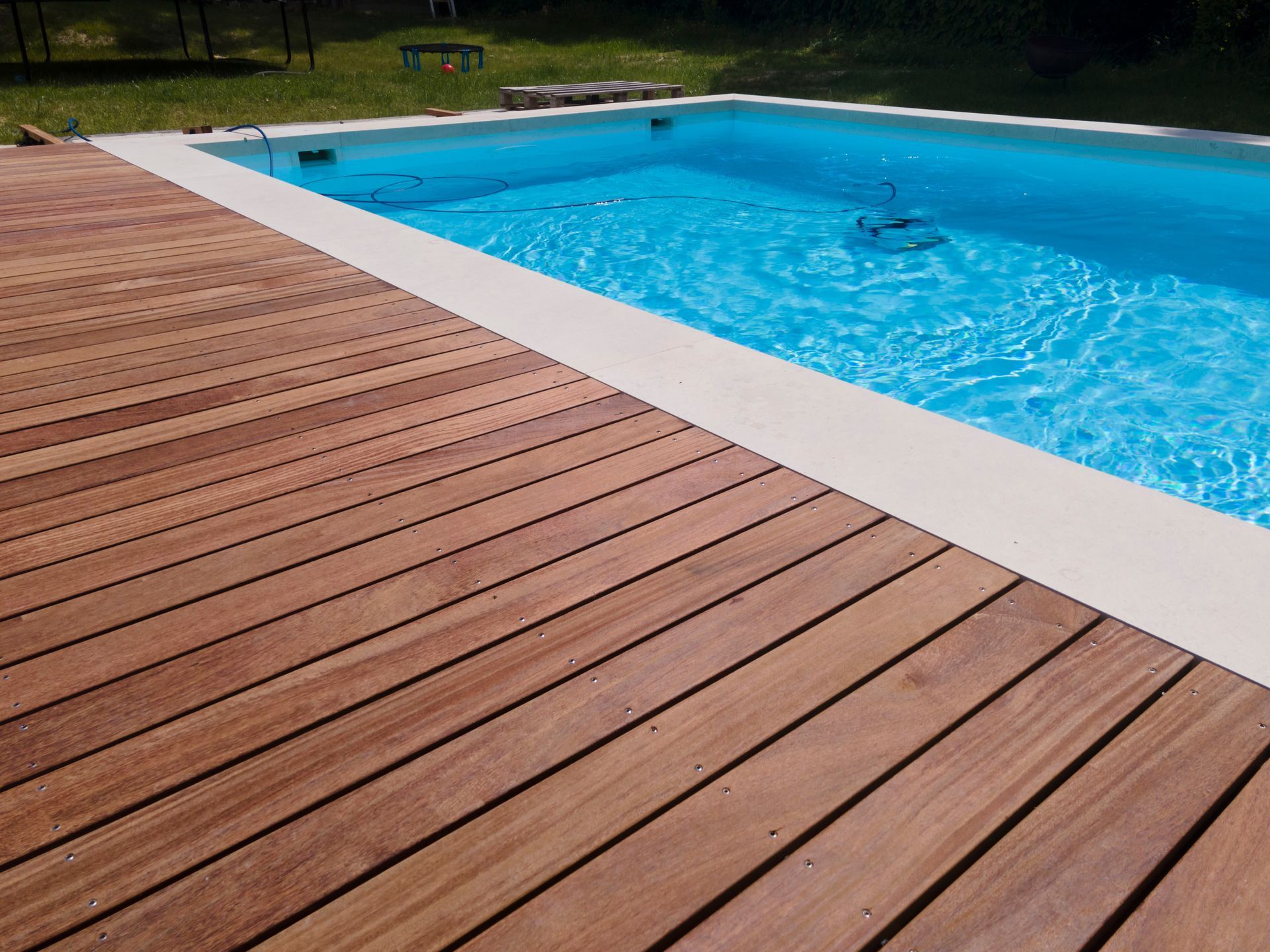 Wooden deck alongside a rectangular swimming pool with blue water.