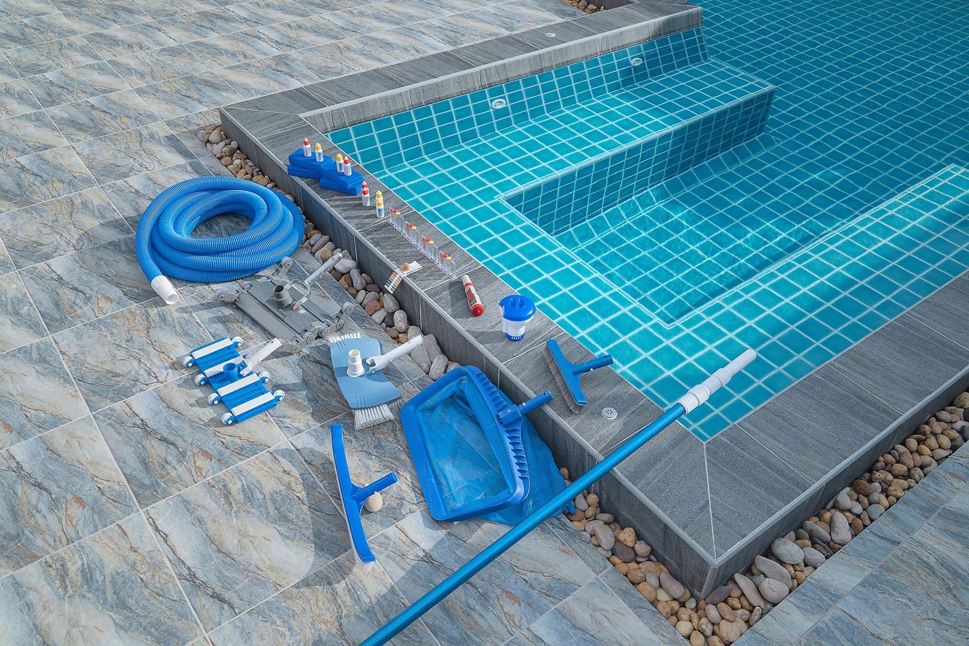 Pool and cleaning supplies arranged on a tiled surface beside a turquoise-tiled pool with steps.