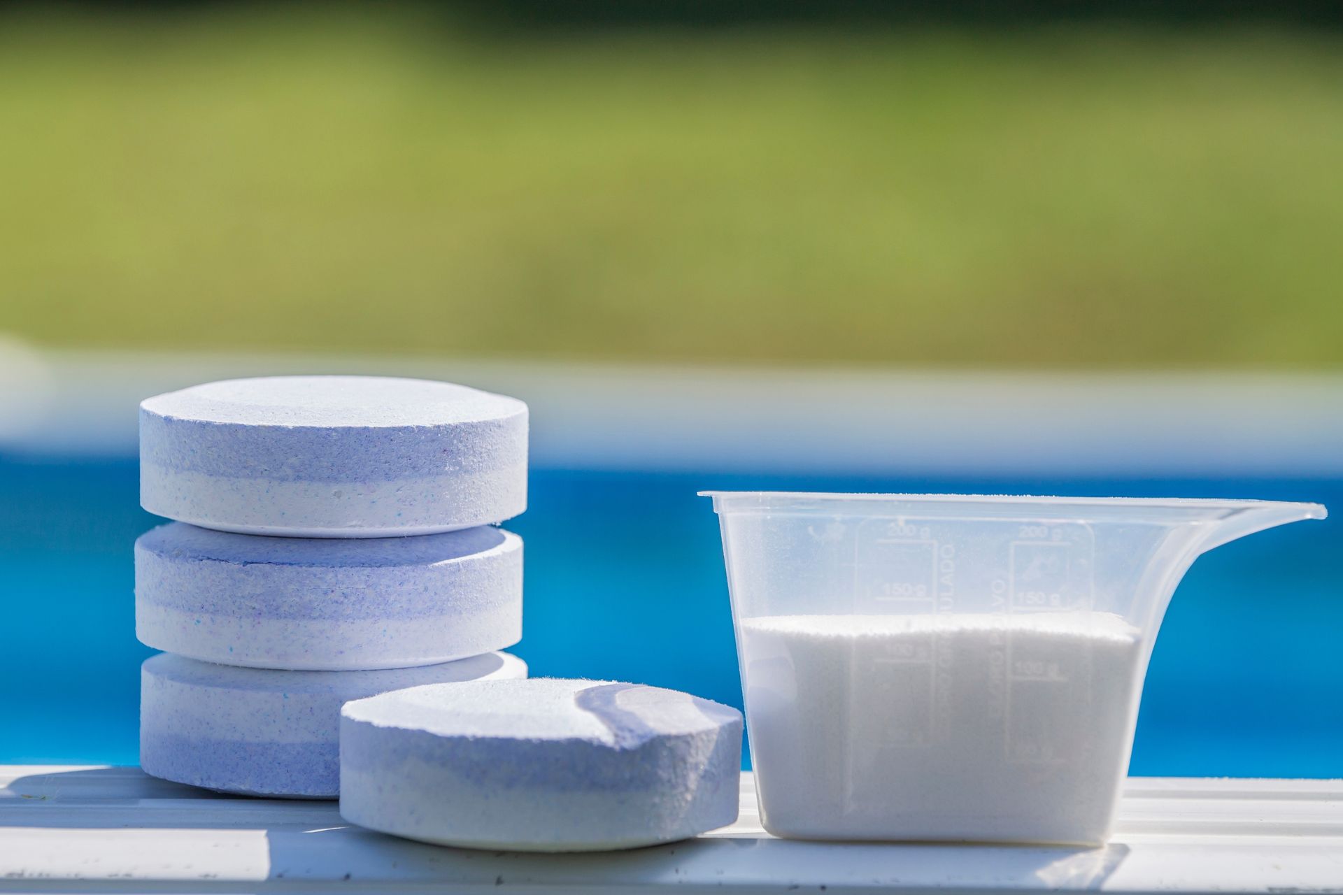 Pool chlorine tablets and powder next to a pool.