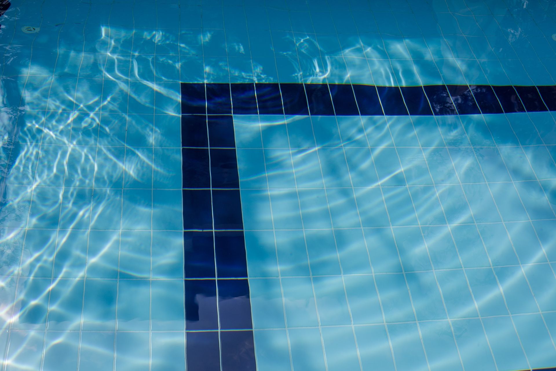 Blue water surface in a swimming pool, visible tiles with a dark blue border.