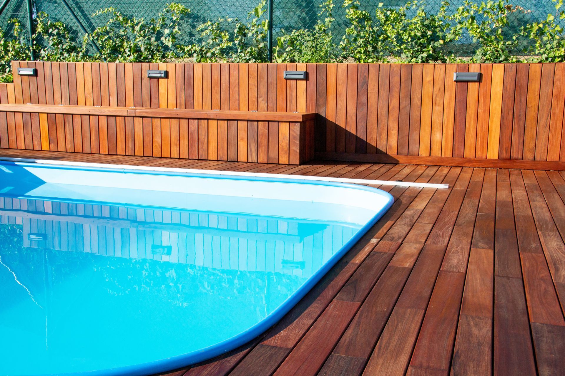 Swimming pool with wooden deck and fence, blue water, sunny day.