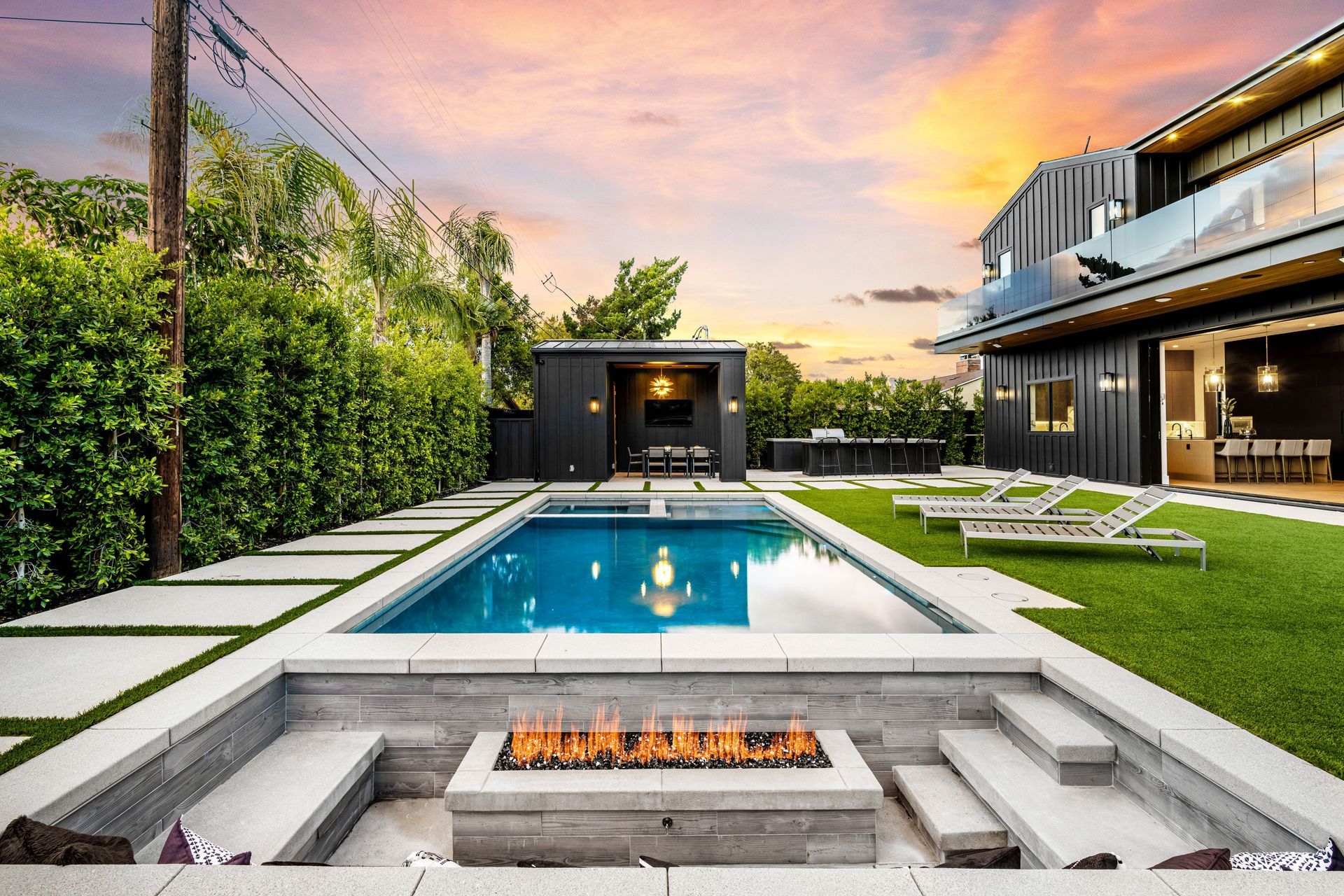Pool with fire pit and modern home at sunset.