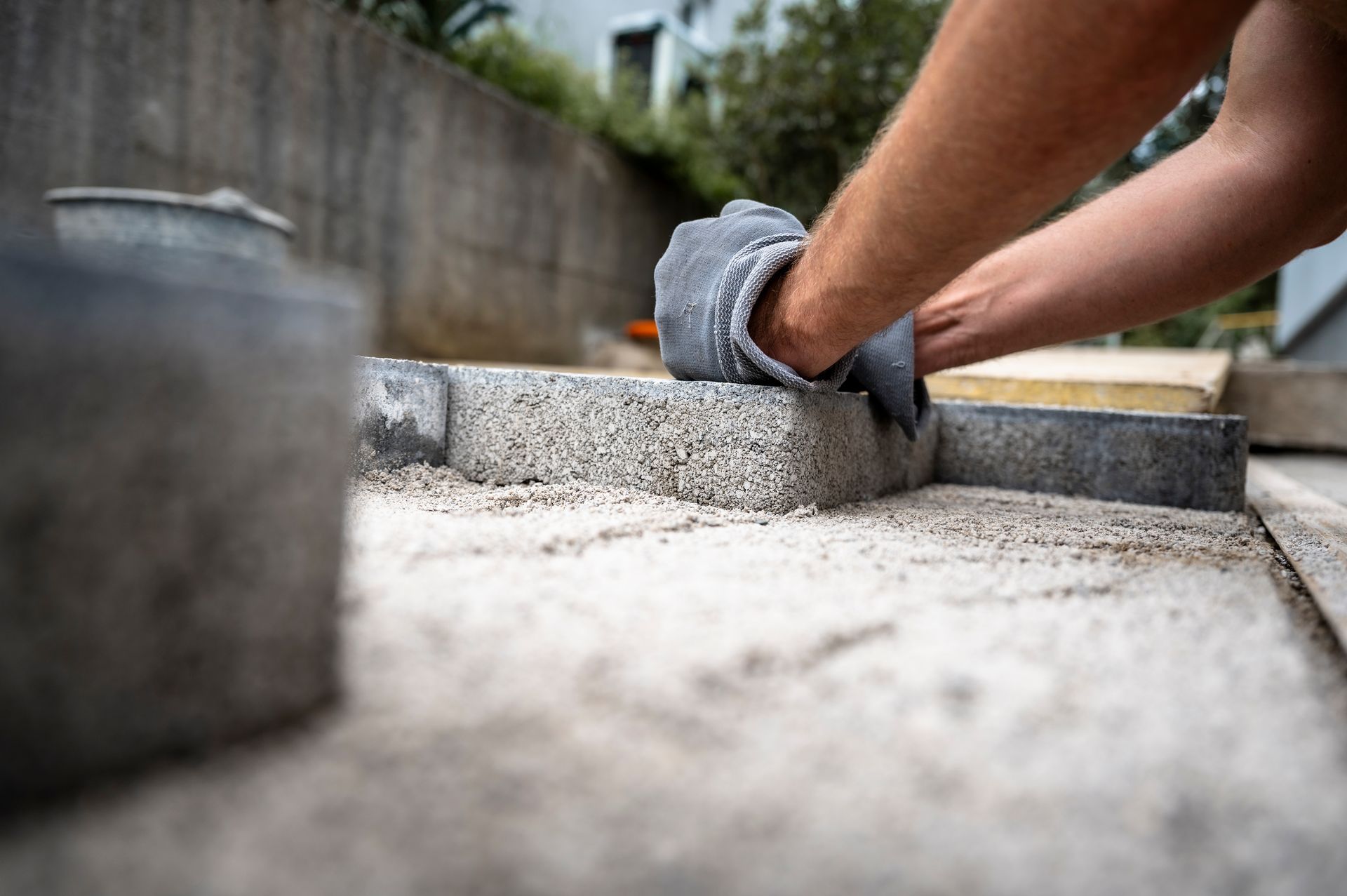 Person wearing gloves, leveling paving stone on a bed of sand outdoors.