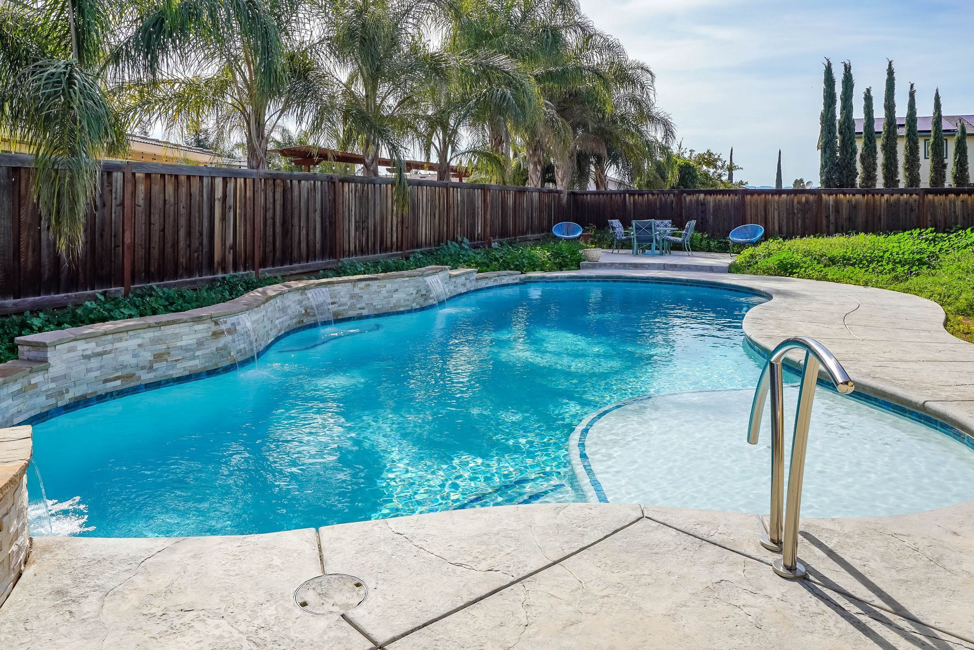 Empty rectangular swimming pool under construction, concrete border, brown fence and yard in background.