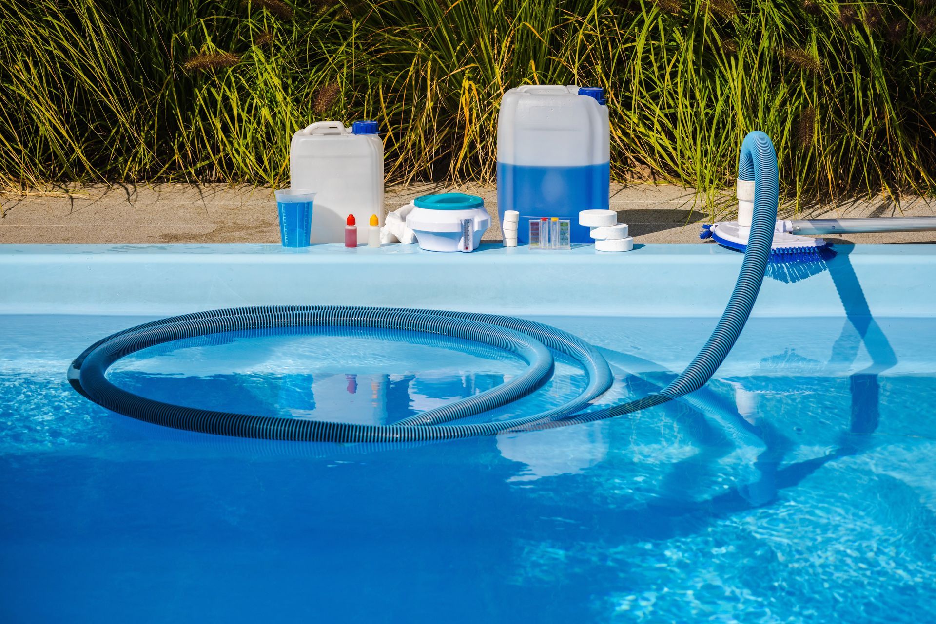 Pool cleaning equipment on a pool edge: hose, brush, chemicals in containers, and a blue pool.