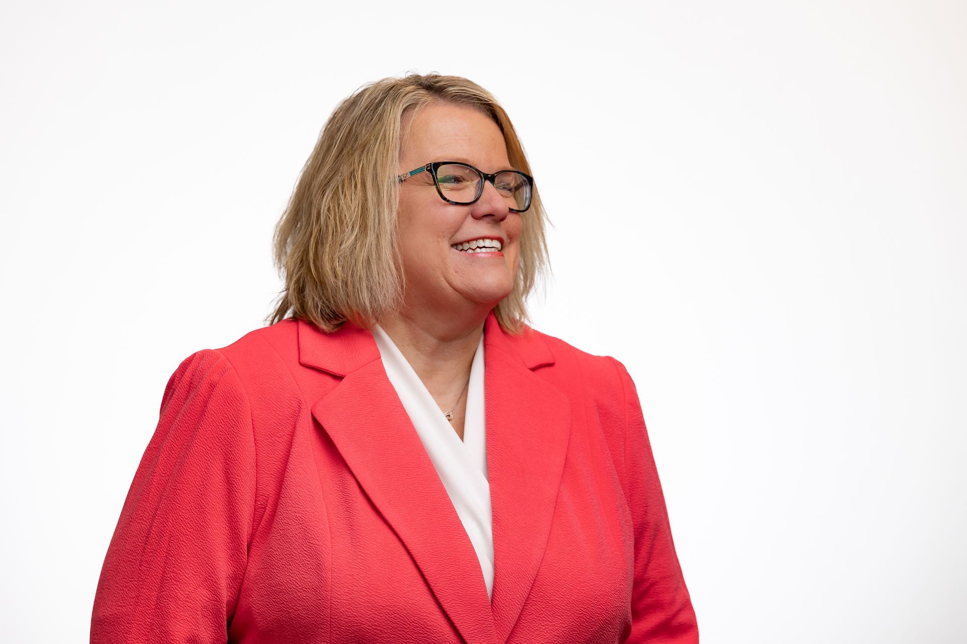 Dr. Celina in red blazer, glasses, smiling, white shirt, against a white background.