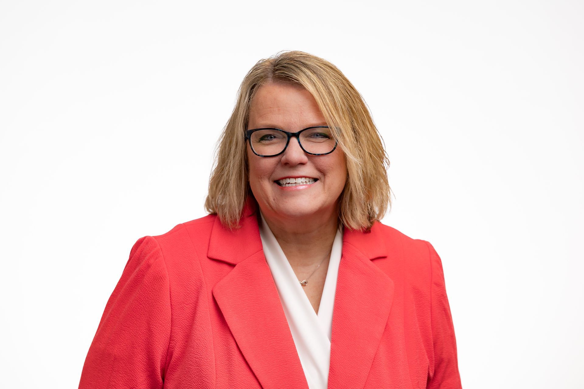 Dr. Celina with blonde hair, wearing glasses and a red blazer, smiling, against a white background.