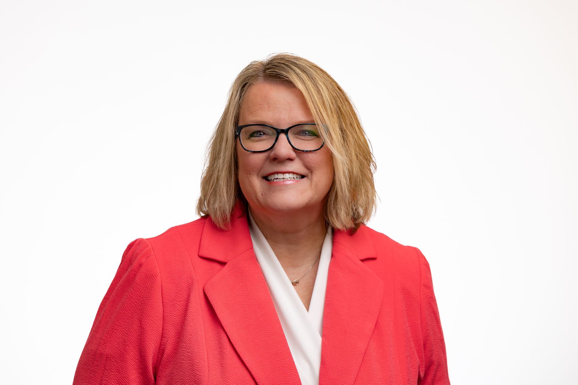 Dr. Celina in glasses smiles, wearing a red blazer and white shirt, against a white background.