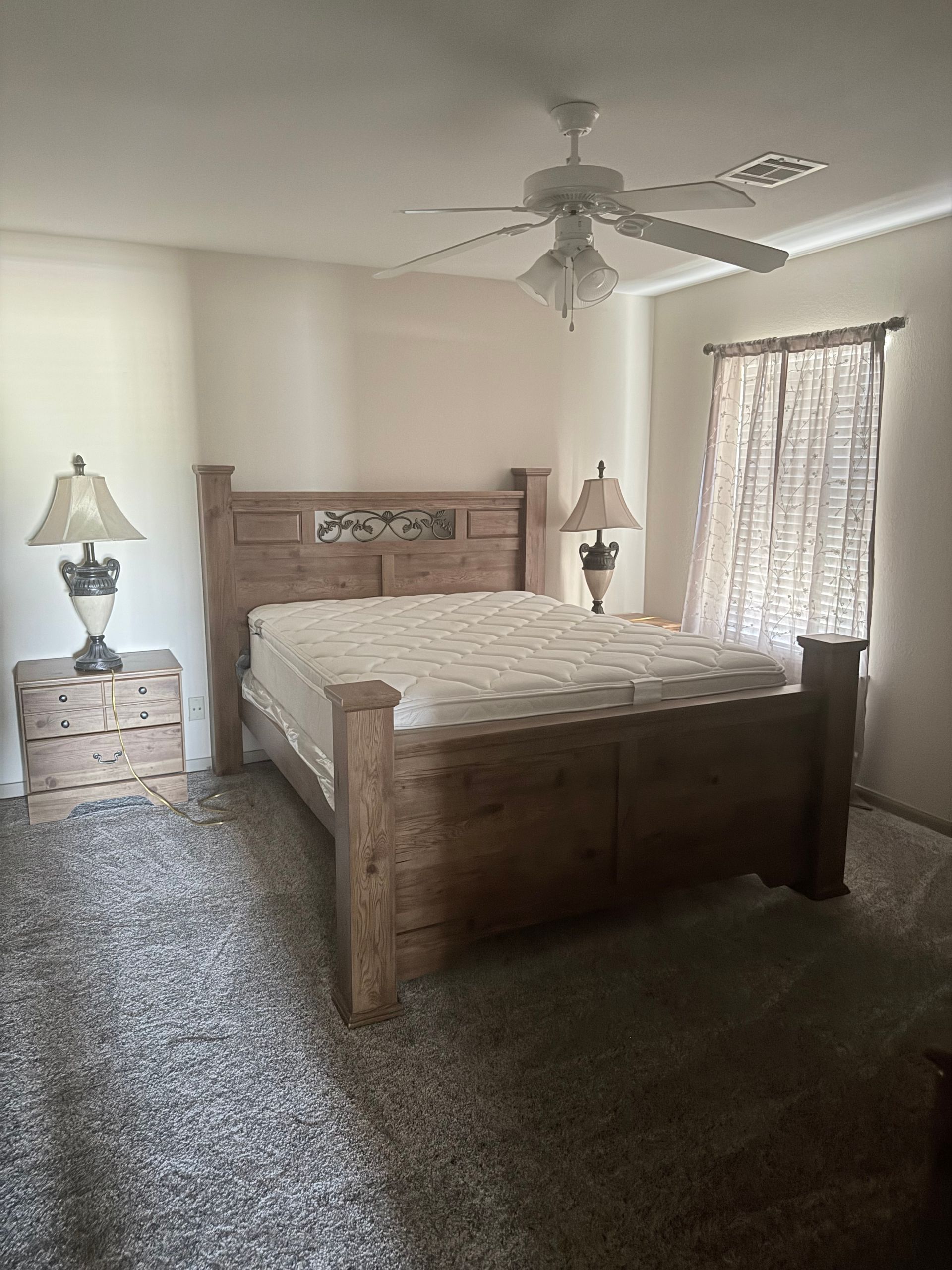 Bedroom with a wooden bed, two nightstands, lamps, window with curtains, and a ceiling fan.