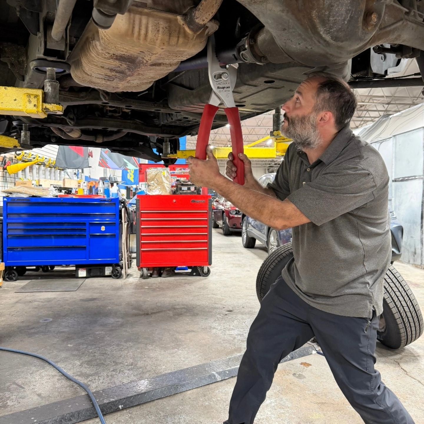 Mechanic using large pliers to cut a car exhaust pipe, working under vehicle in a shop | La Saga Auto