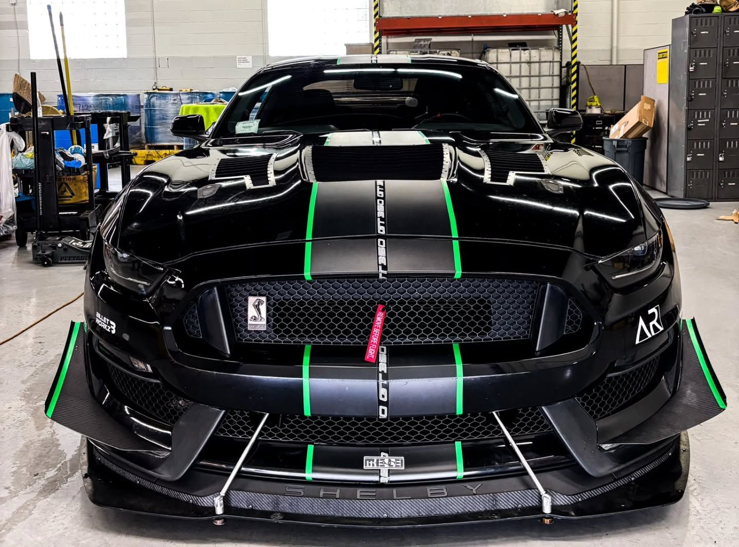 Black Ford Mustang with green racing stripes and modifications, indoors  | La Saga Auto