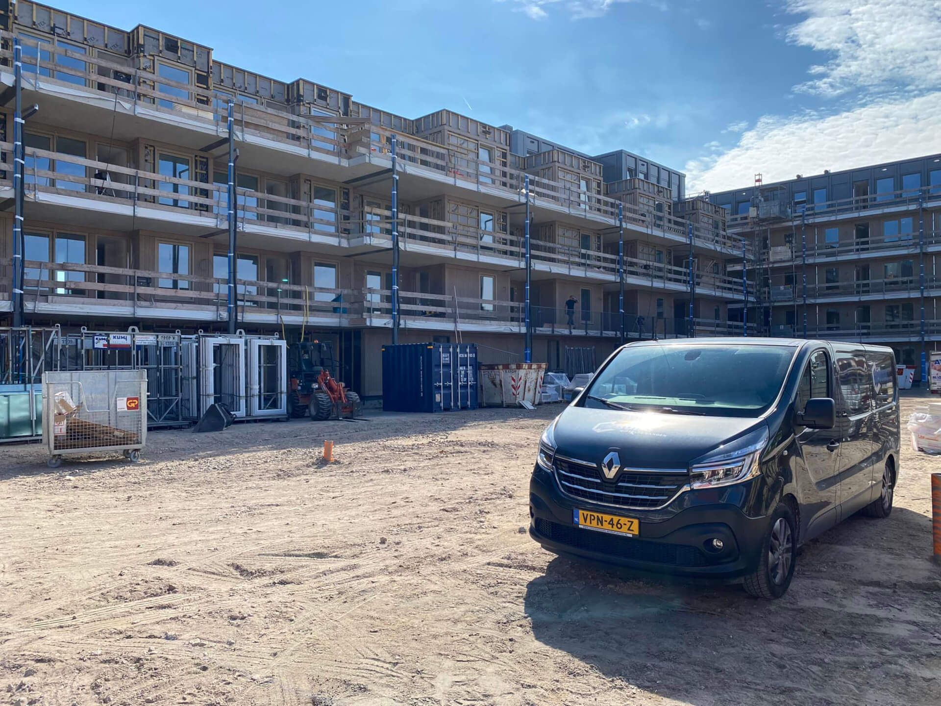 Voor een gebouw in aanbouw staat een zwart busje geparkeerd.