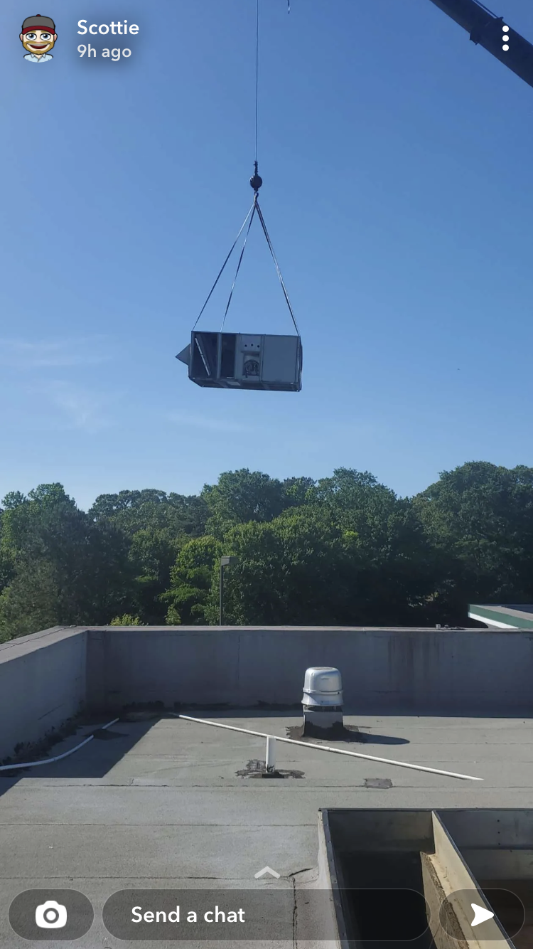 A crane is lifting an air conditioner from the roof of a building.