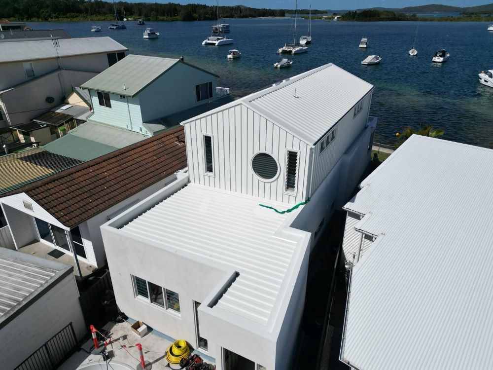 An Aerial View of a White House Next to a Body of Water — Lake Valley Roofing in Broadmeadow, NSW