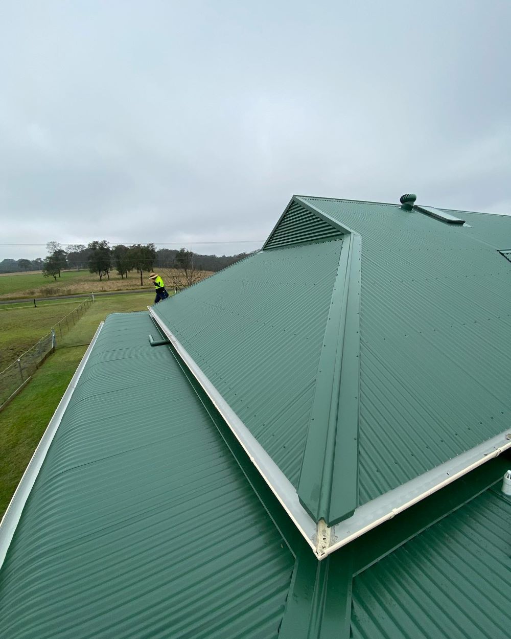 A Man is Standing on Top of a Green Roof — Lake Valley Roofing in Cessnock, NSW