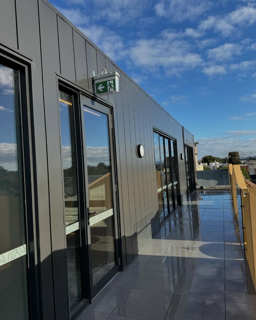 A Building With a Green Exit Sign on the Side of It — Lake Valley Roofing in Toronto, NSW