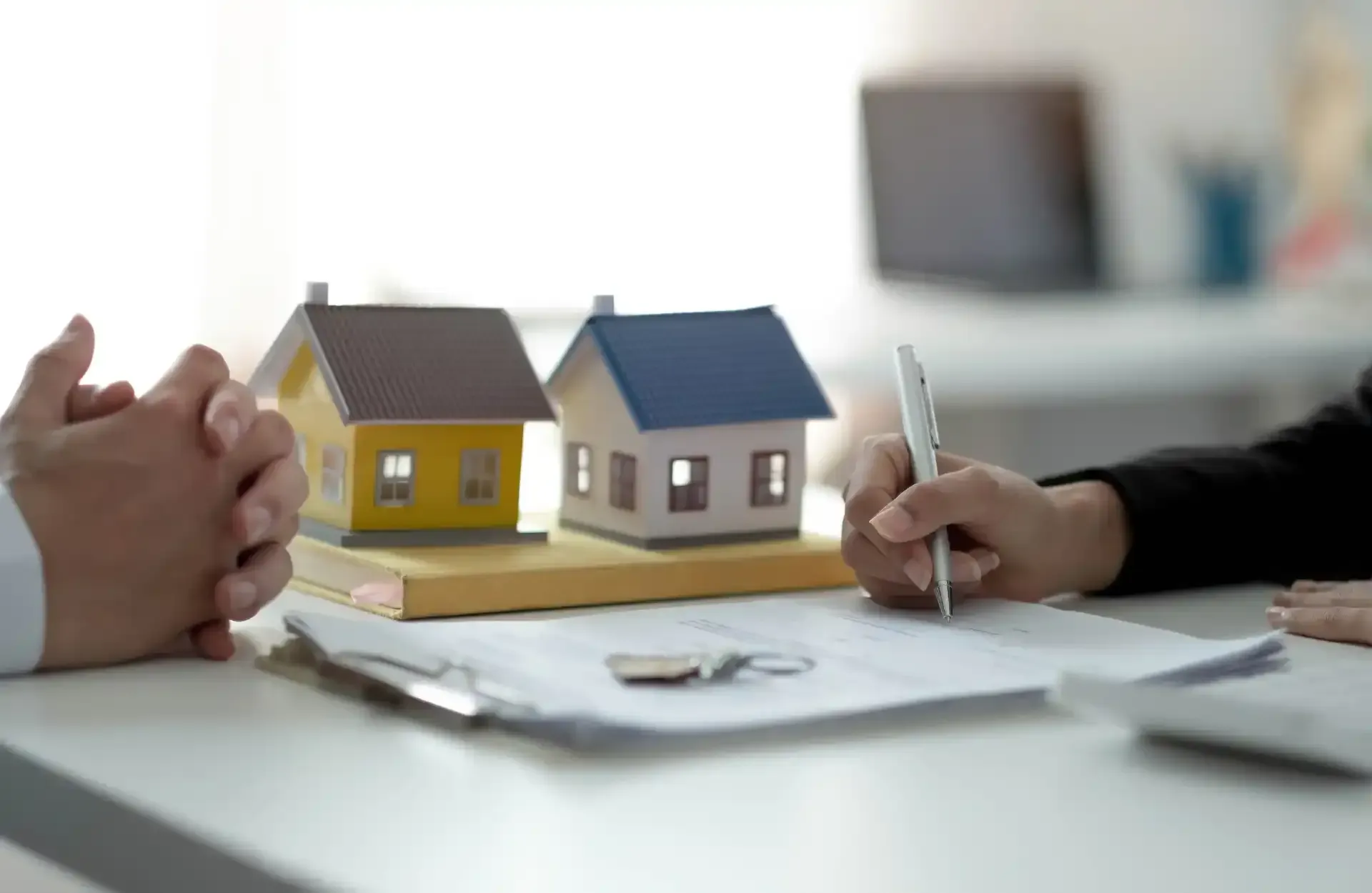 Buyer and lawyer signing a sales agreement with miniature houses on a table.