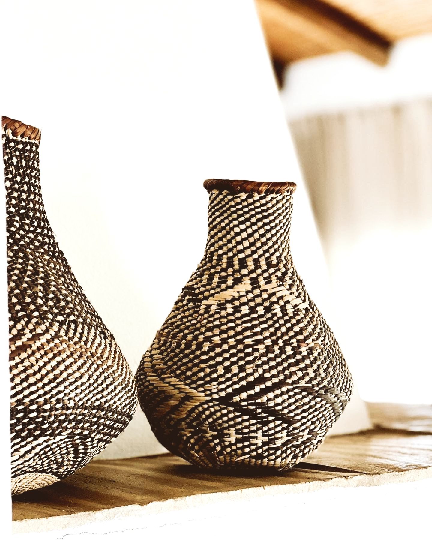 Two woven black and white patterned vases on a wood shelf, against a white backdrop.