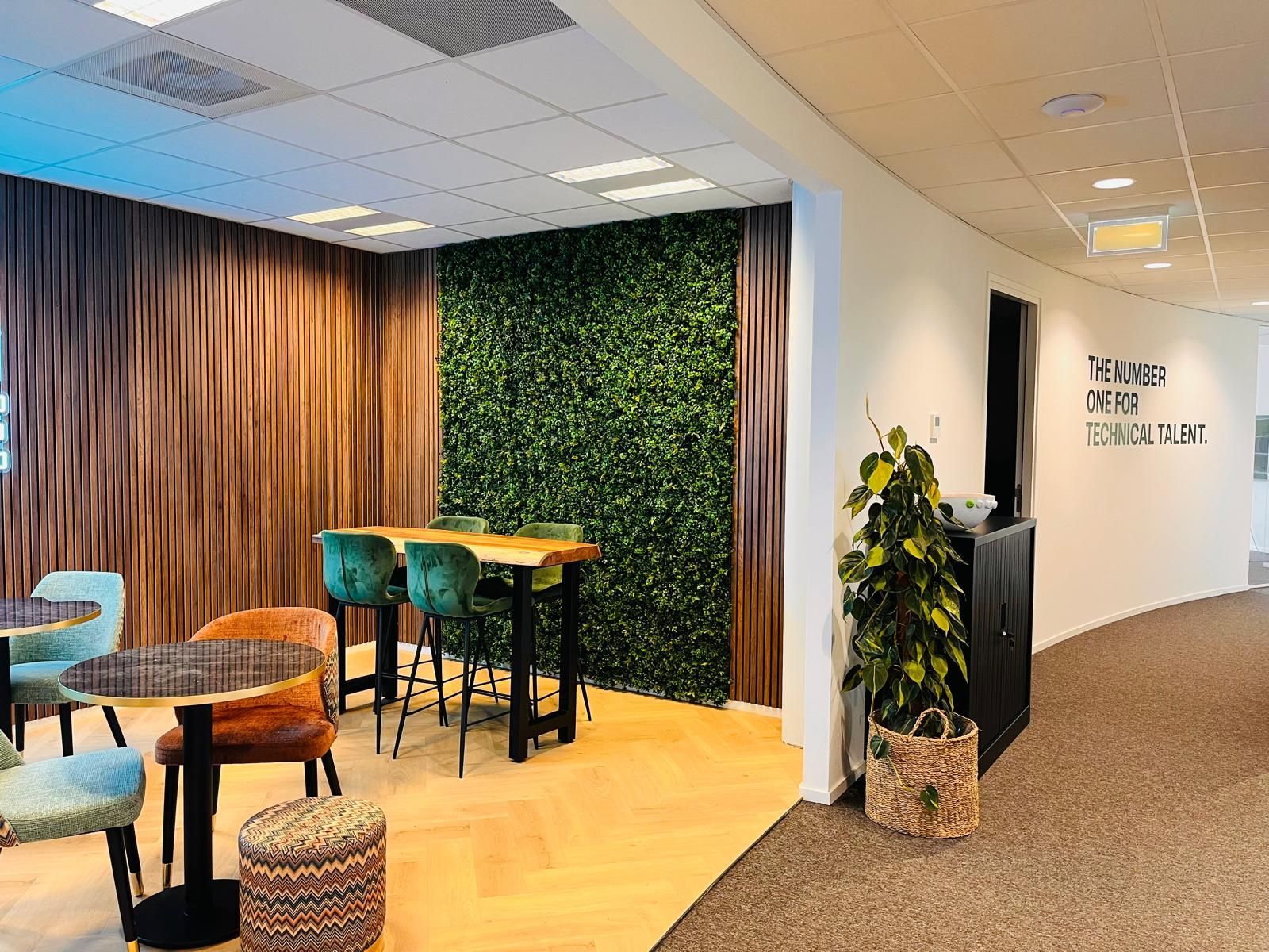 A modern office lounge with a green wall, high-top table, and colorful chairs.