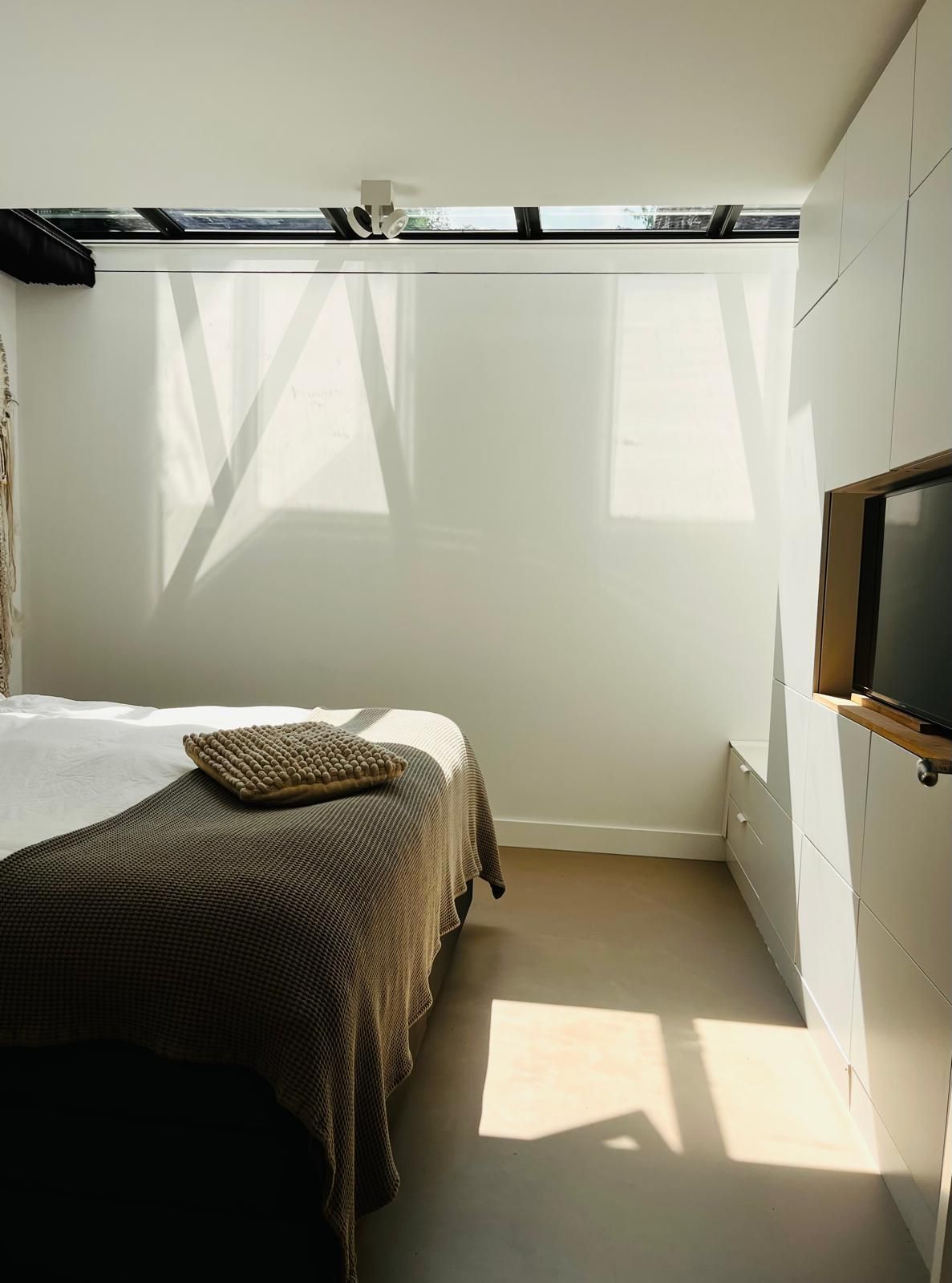 Bedroom with bed, sheer blinds, and sunlight casting shadows.