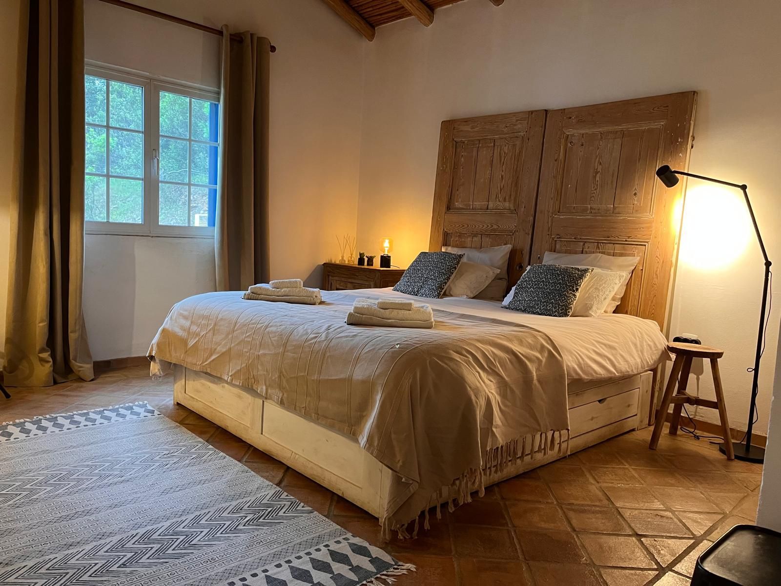 Cozy bedroom with a king-size bed, wooden headboard, rug, and a floor lamp beside a small stool.