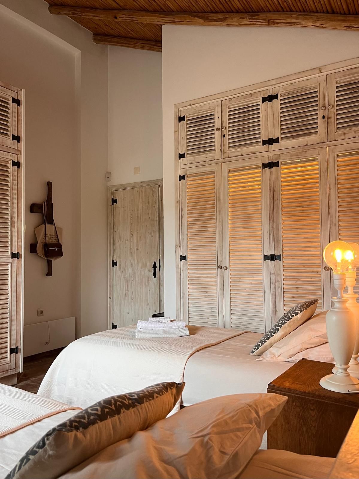 Bedroom with two beds, white shutters, neutral colors, cozy and inviting.