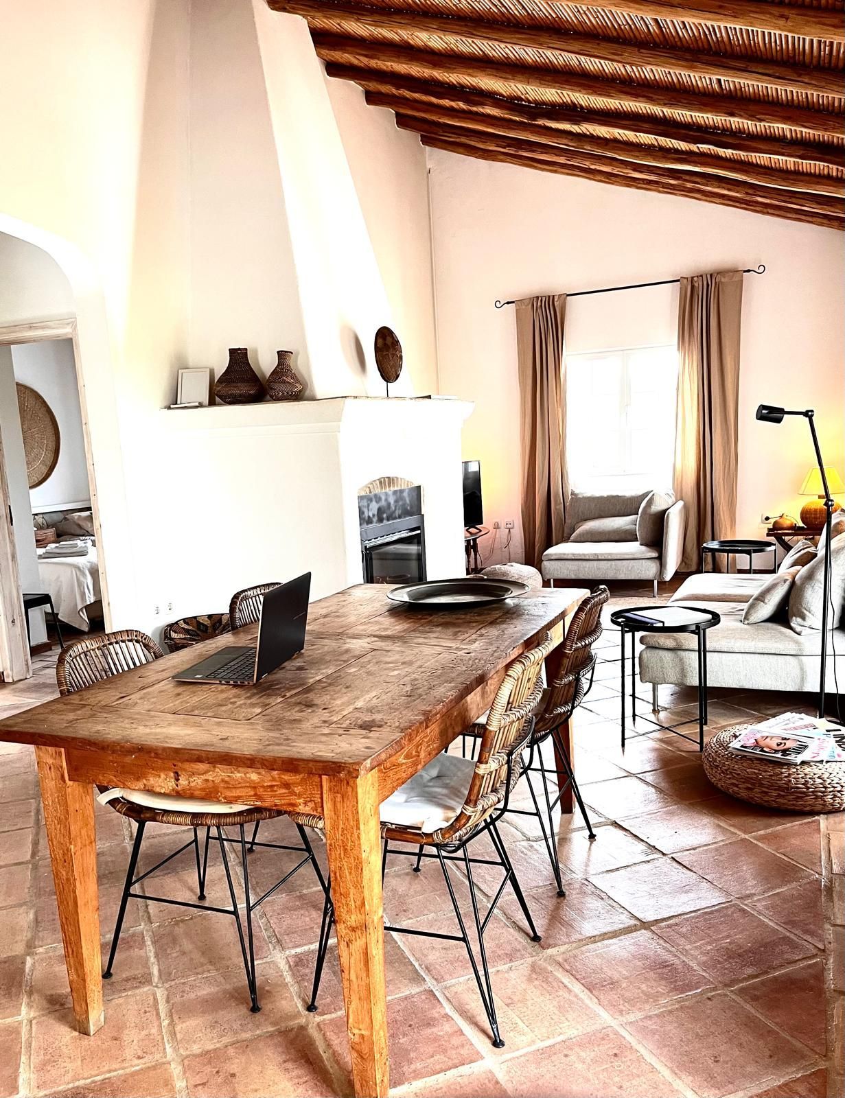 Rustic dining room with a wooden table, chairs, fireplace, and terracotta tile floor.