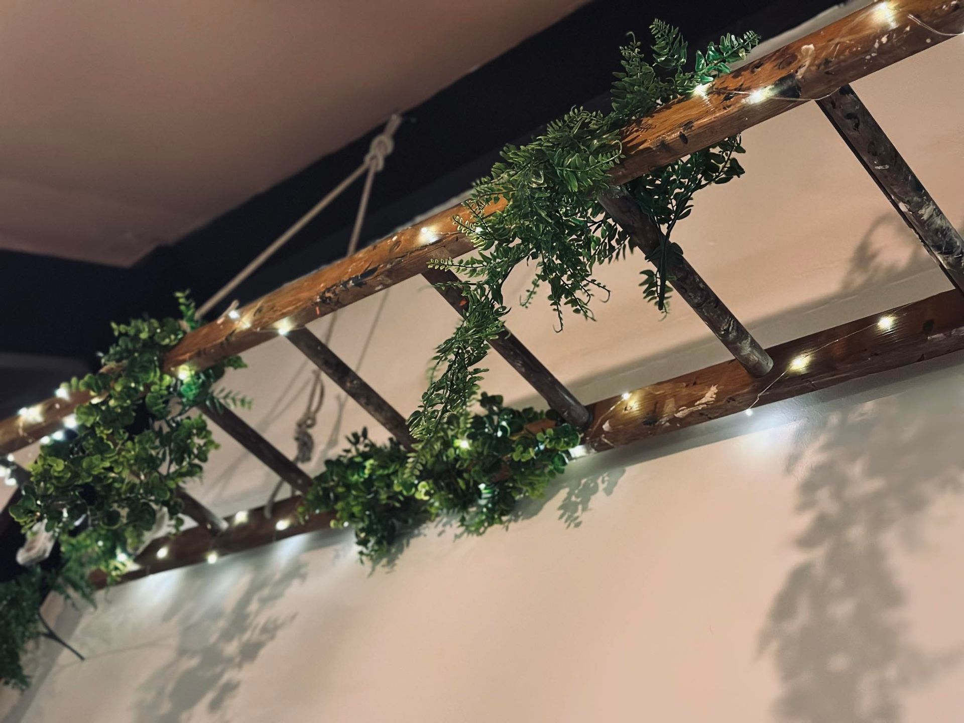 A wooden ladder is decorated with greenery and lights