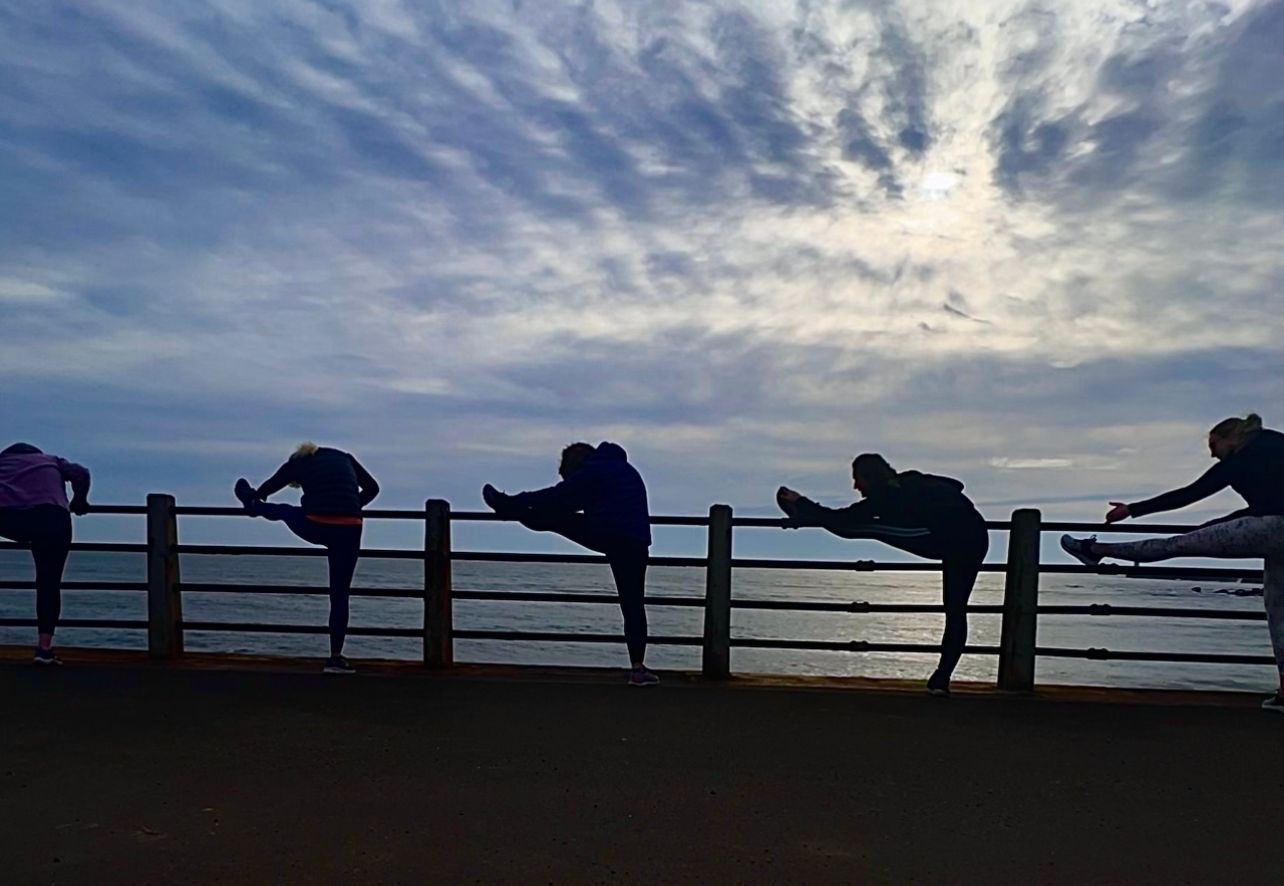 A group of people stretching on a fence overlooking the ocean