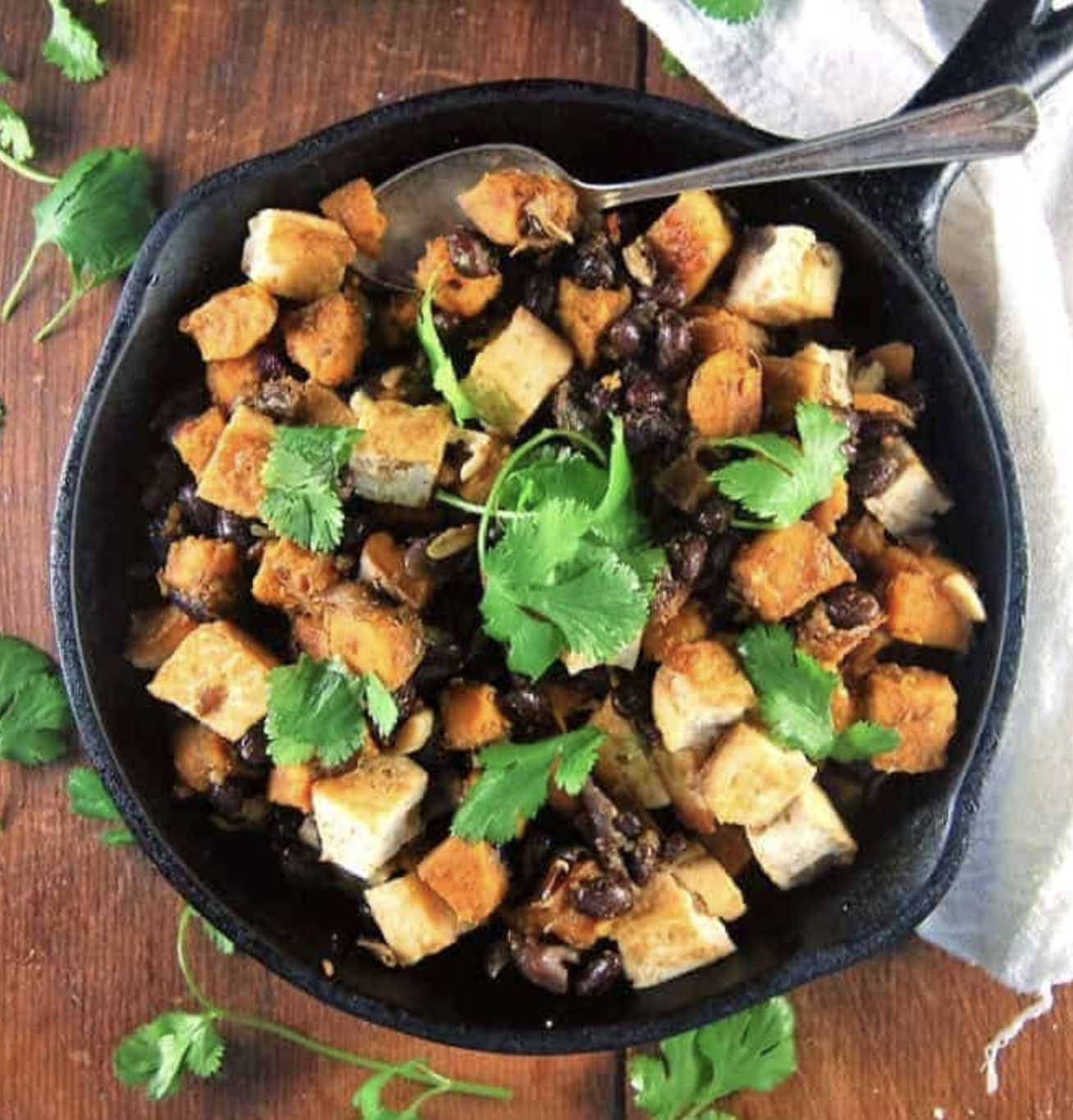 A skillet filled with food and a spoon on a wooden table.