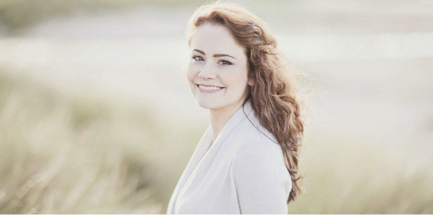 A woman is standing in a field of tall grass and smiling.