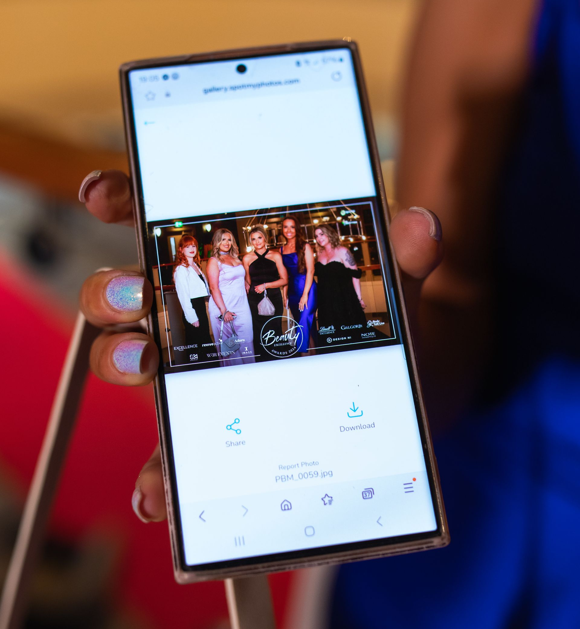 Smartphone displaying a photo of five women in formal wear; sharing and download buttons visible. Event Photography.