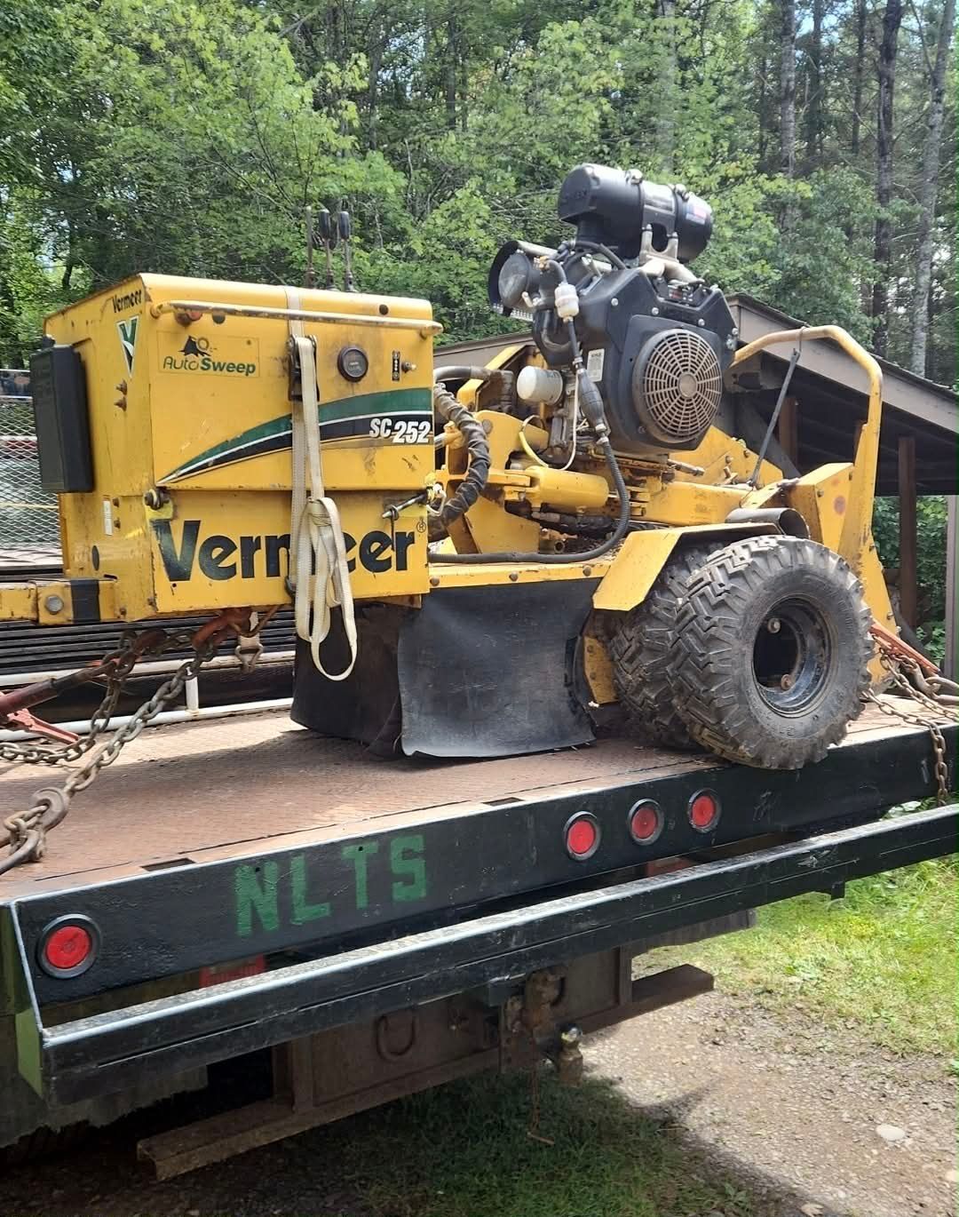Yellow stump grinder grinding a tree stump in a yard, wood chips flying.