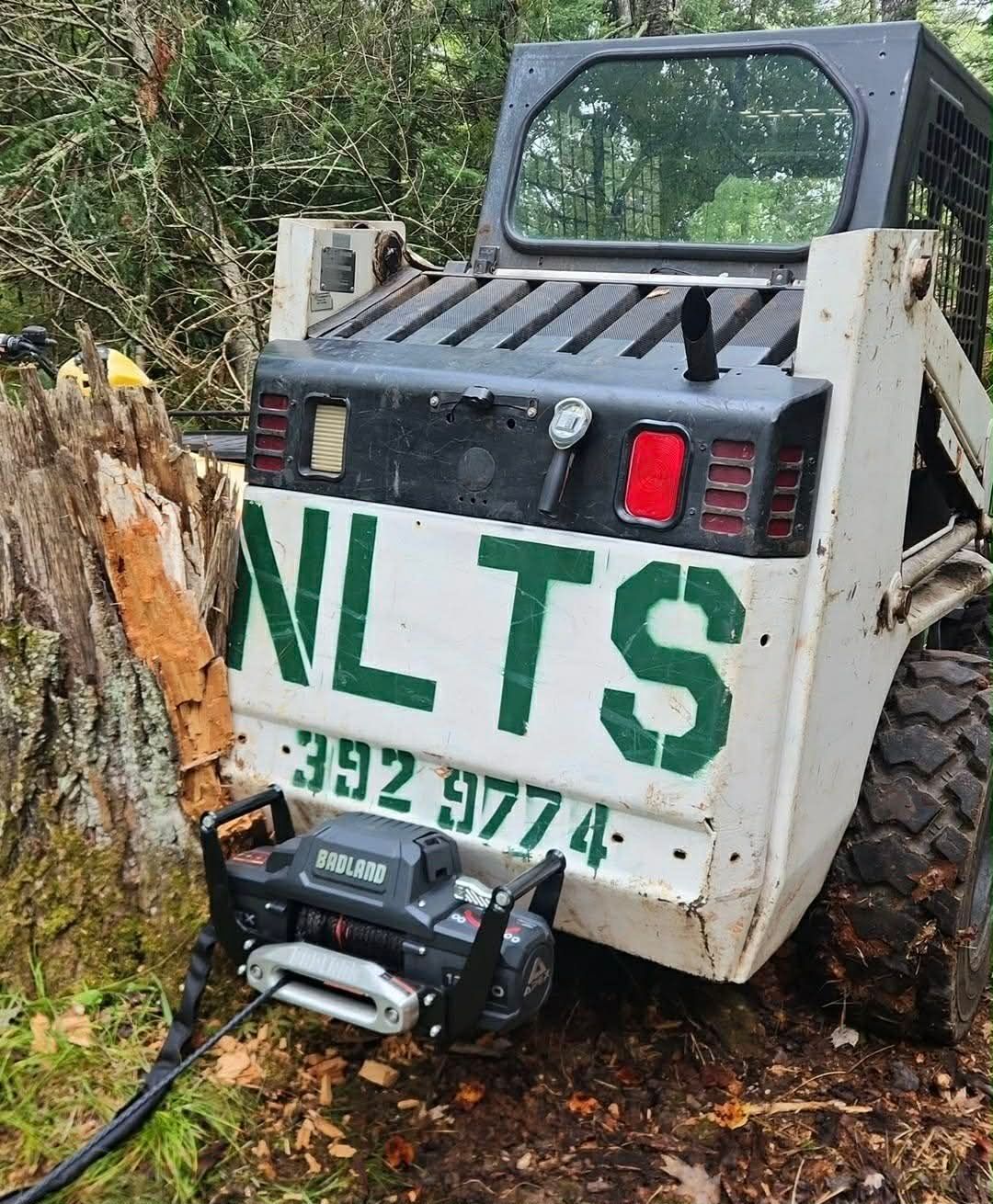 Three workers in green trimming trees near a building, surrounded by cut branches.