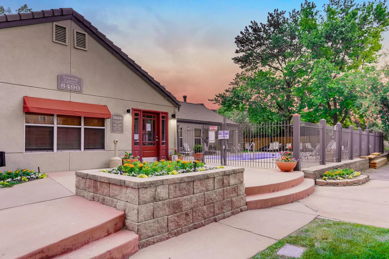 Leasing center with red door and planters, gated pool area visible in the background.